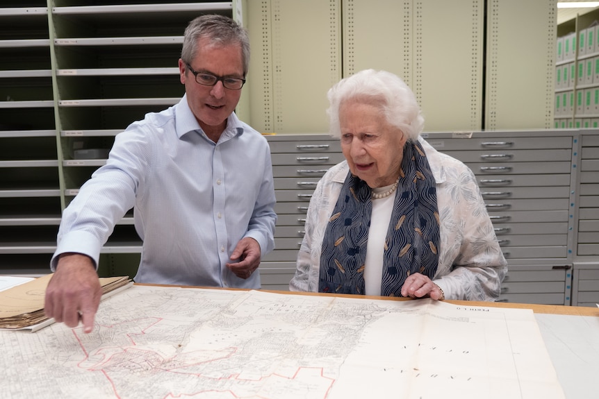 Woman with white hair and man in blue shirt look at old documents on a table
