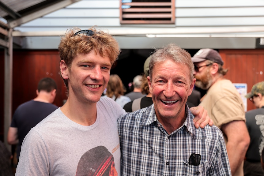 Two men stand smiling with arm around each other in busy beer garden