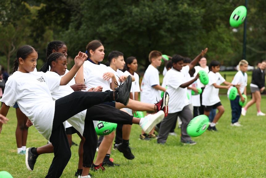 Children in line kick footballs
