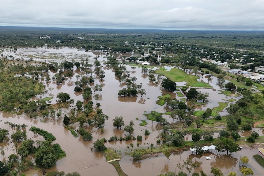 An aerial photo shows puddles of brown floodwaters across parts of a rural town.