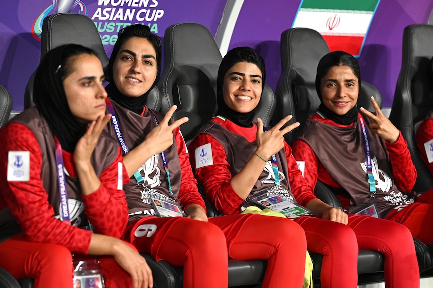 Members of the Iran women's football team flash peace signs as they sit on the bench
