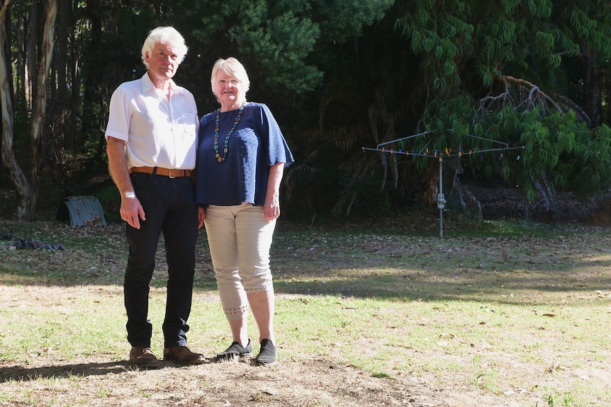 man in white shirt and black pants next to woman with dark blue top and slacks standing in bush area