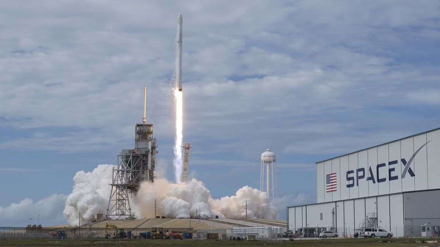 A rocket launching to space next to a SpaceX building.