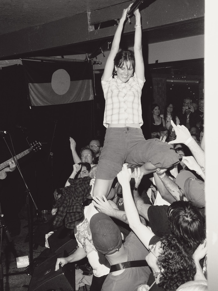 Black and white photo of a chaotic music event with a young man crowdsurfing across a lively crowd