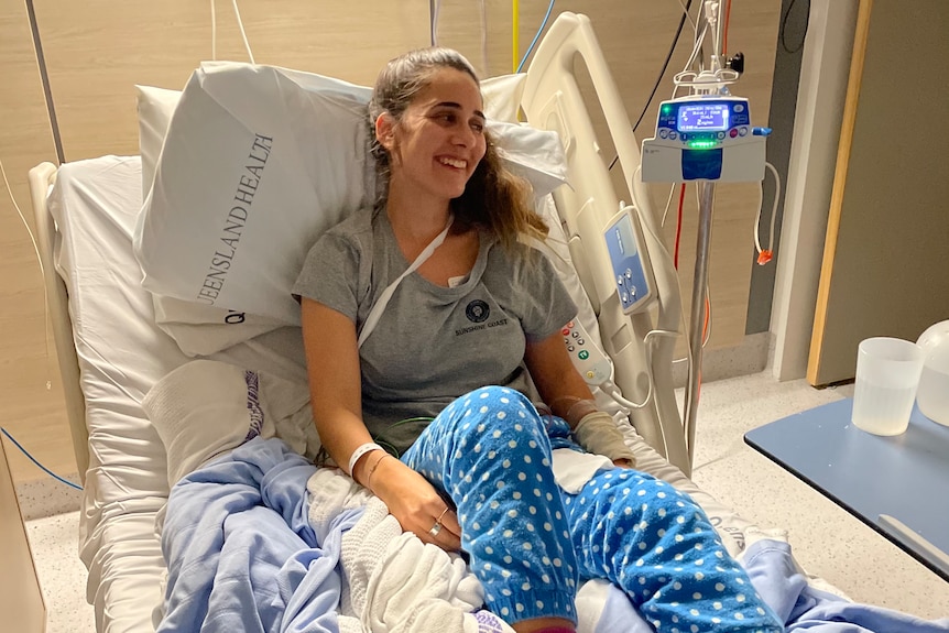 A woman in pyjamas sitting in a hospital bed and smiling