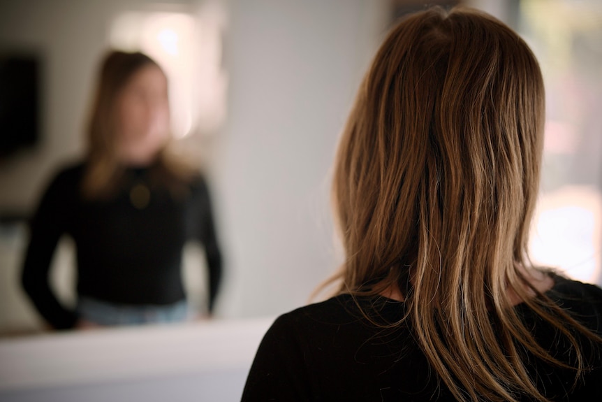 A blurred out image of a woman looking into a mirror.