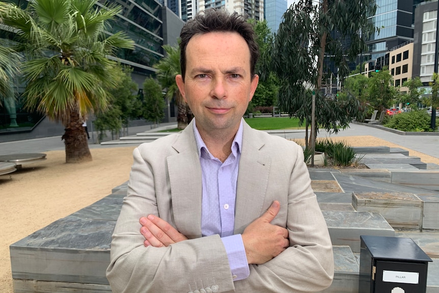 A man folds his arms and looks directly at the camera.