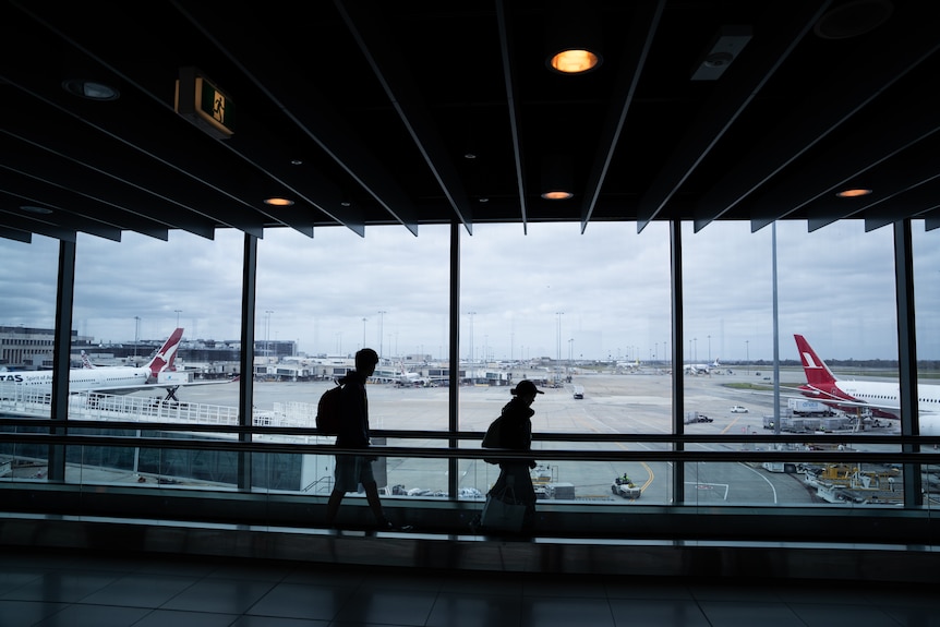 Passengers walk in front of a plane at an airport
