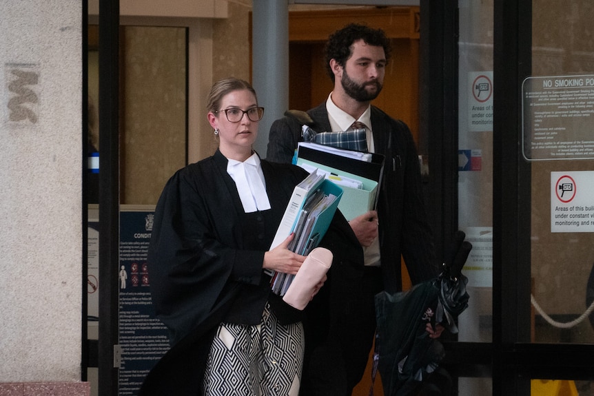 A female barrister in robes and a male solicitor in a suit leaving a building