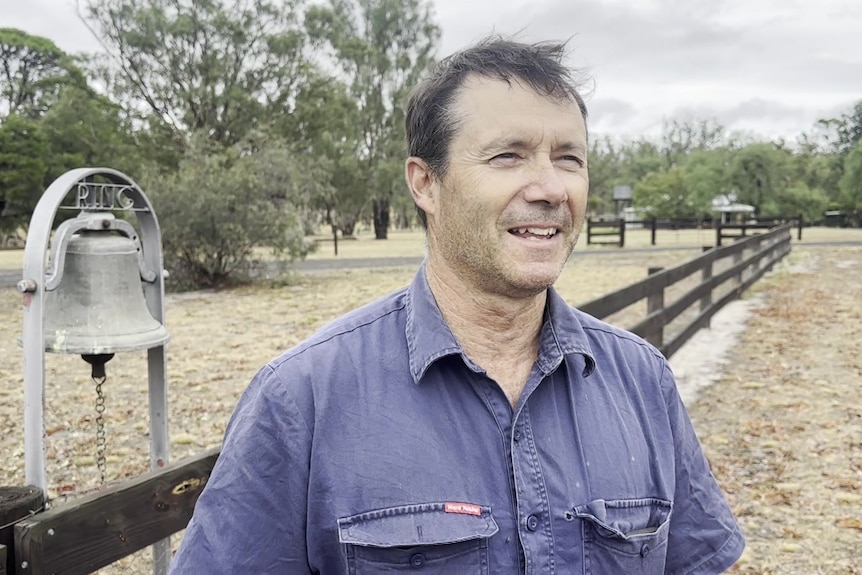 A man stands smiling on a farm as puddles can be seen behind him
