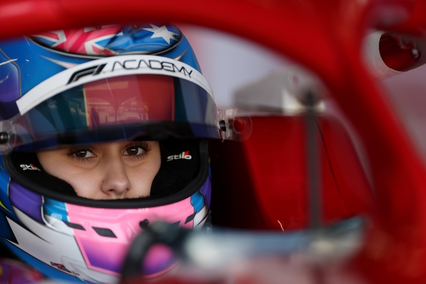 A young woman in a racing helmet looks at the camera.
