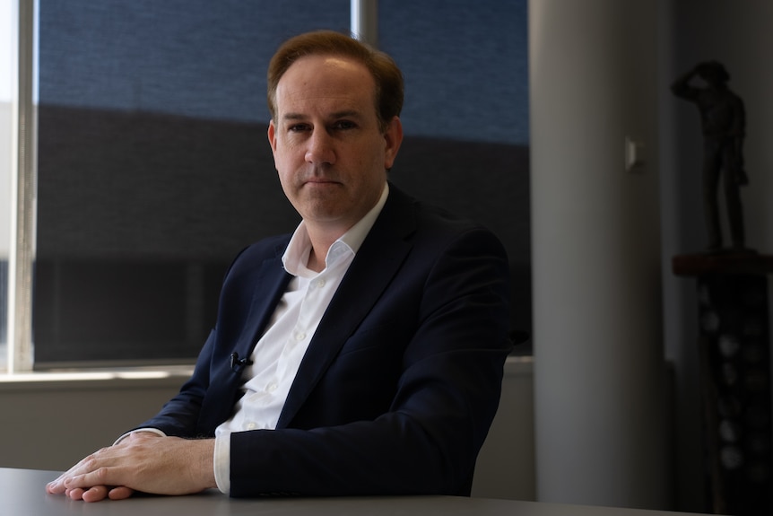 Warren Pearce sits at a table wearing a dark suit jacket and white shirt.