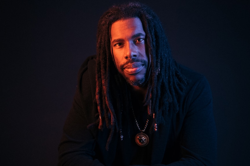 African American man with long dreads poses in darkly lit photoroom