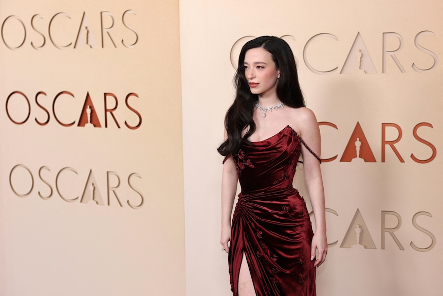 A white woman with long black hair in a red velvet sleeveless dress.