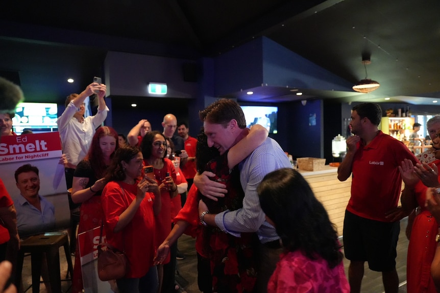 Ed Hugs a woman at a bar, while supporters cheer