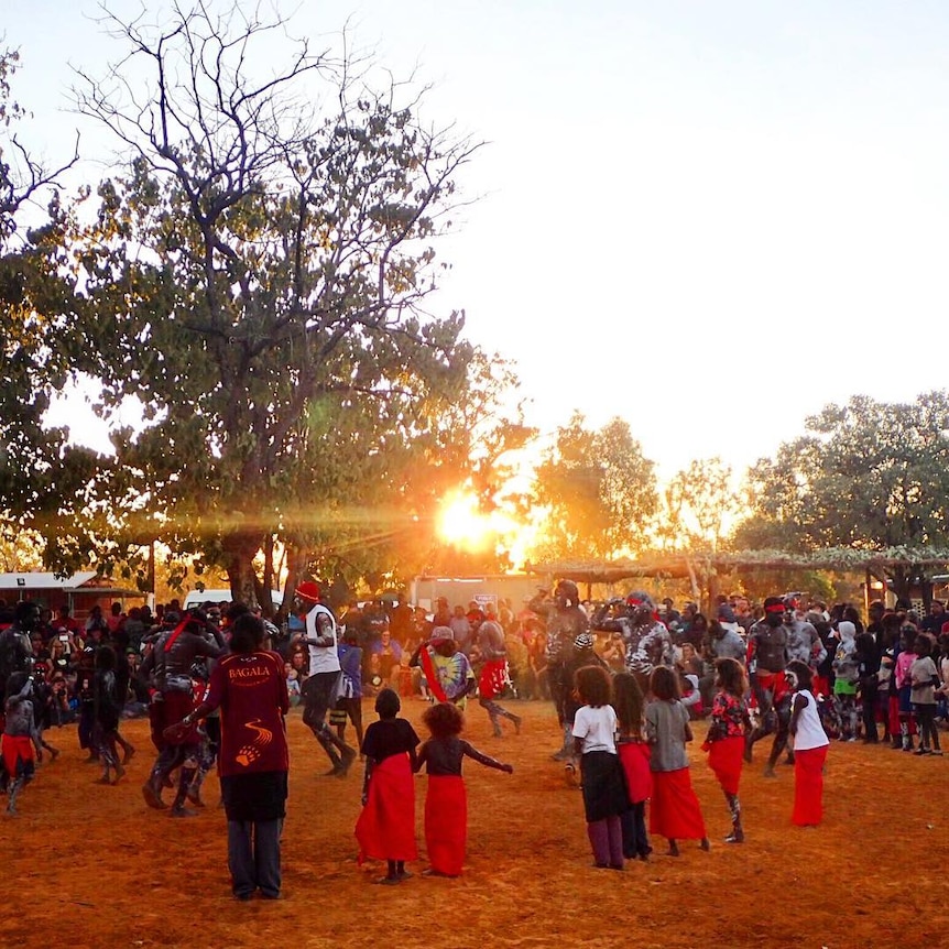 A crowd of people dance as sun begins to set. Trees around.