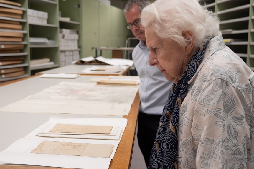 Woman with white hair and man in blue shirt look at old documents on a table