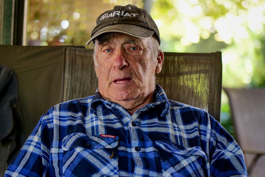 Ron Woodall sits in a chair wearing a blue shirt and black ariat cap