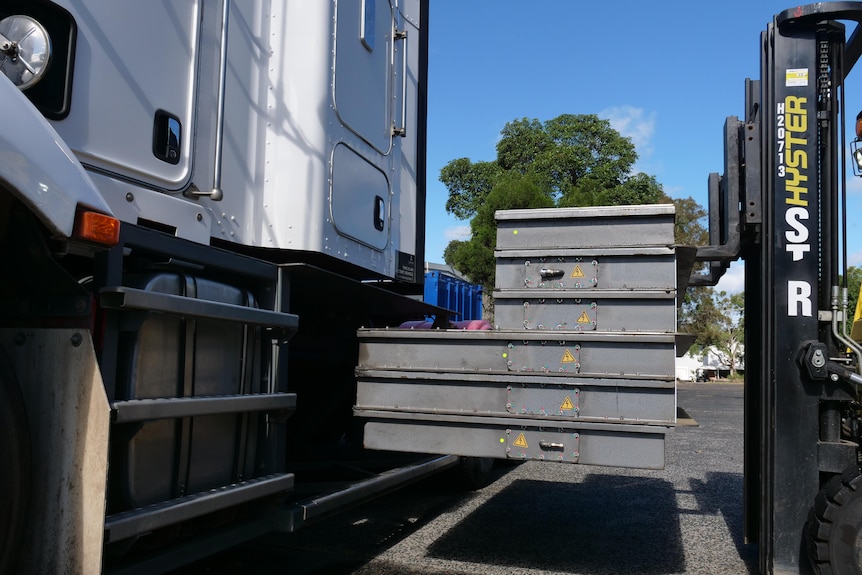 A forklift loading a large battery into the side of a truck.