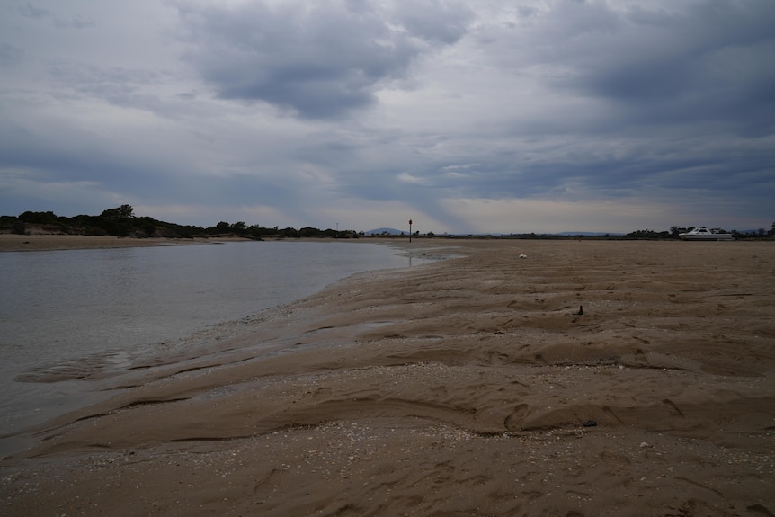The narrow channel, an expanse of sand and a small boat sitting on sand.