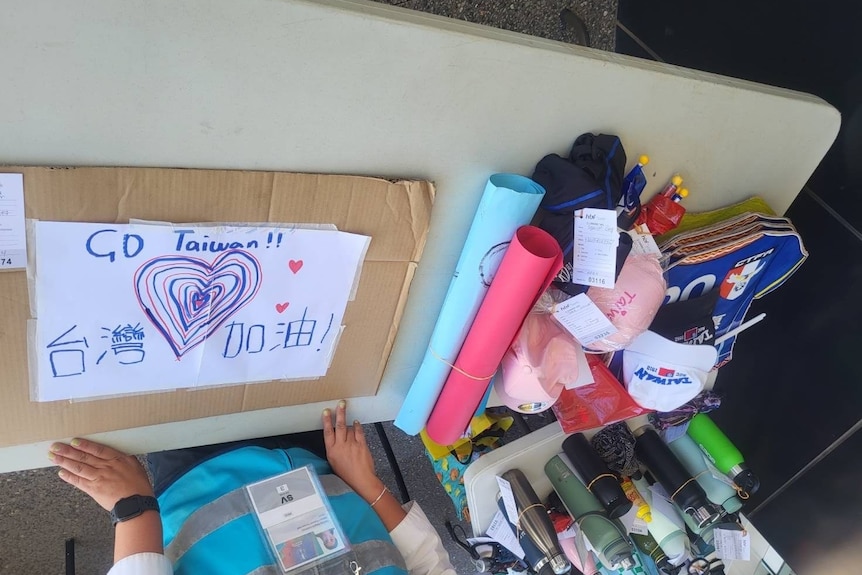 A person leaning over a desk with a cardboard sign that reads: "Go Taiwan"
