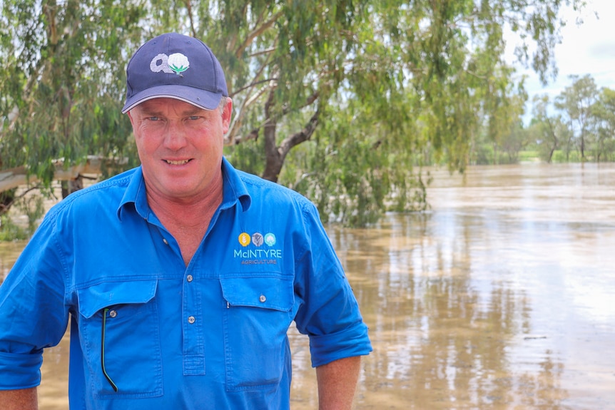 A man in a blue shirt poses in front of a river.