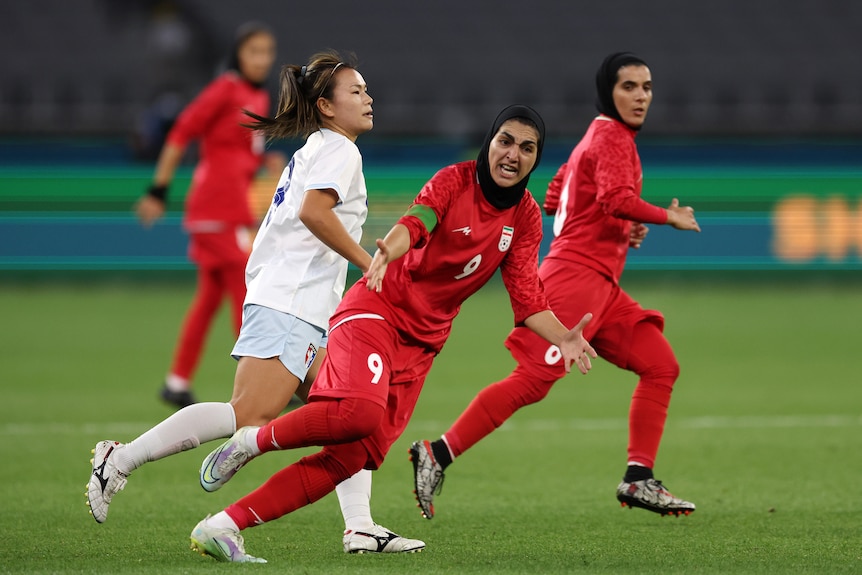 A female Iranian footballer wearing a hijab gesticulates for the ball during a game.
