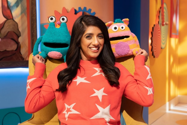 A woman stands with two toys behind each shoulder.