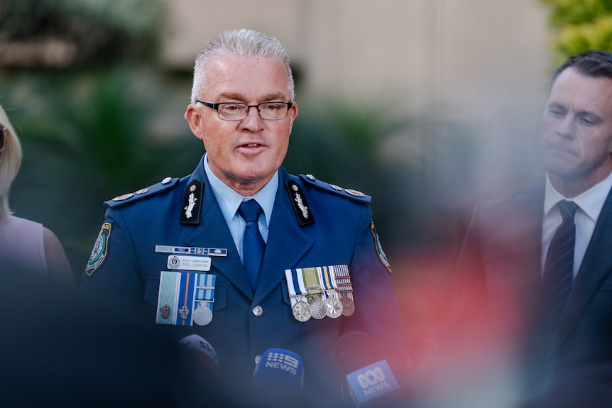 Man in NSW police uniform, blurry people either side of him