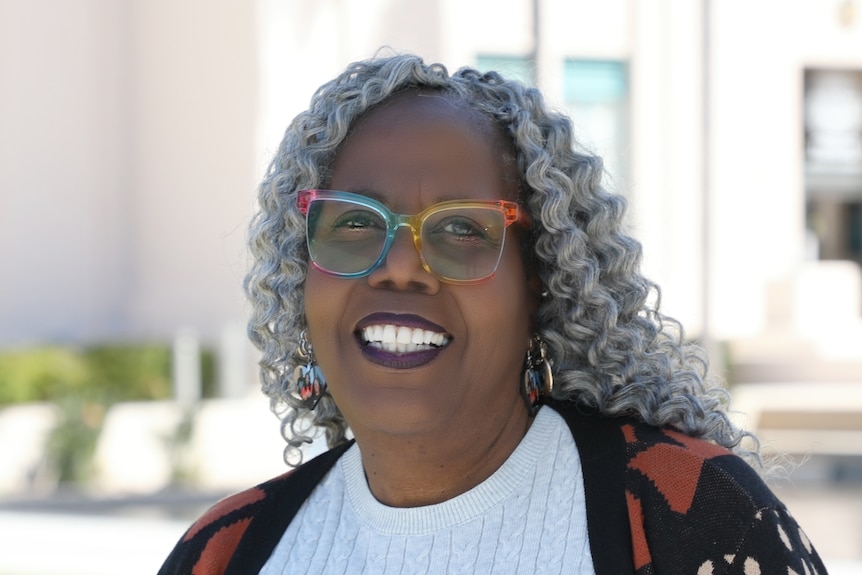 Woman with colourful glasses smiles at camera standing outside