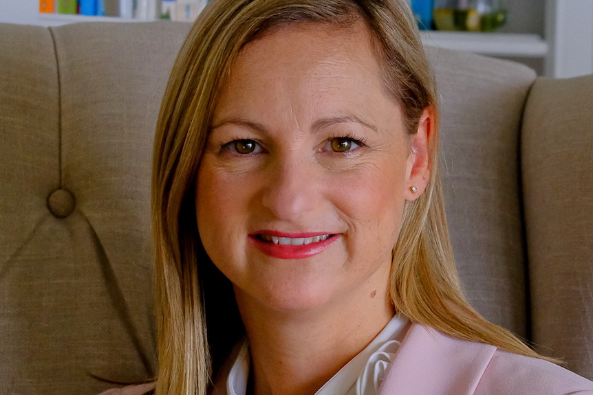 A woman with a pink suit jacket and long blond hair smiling for the camera