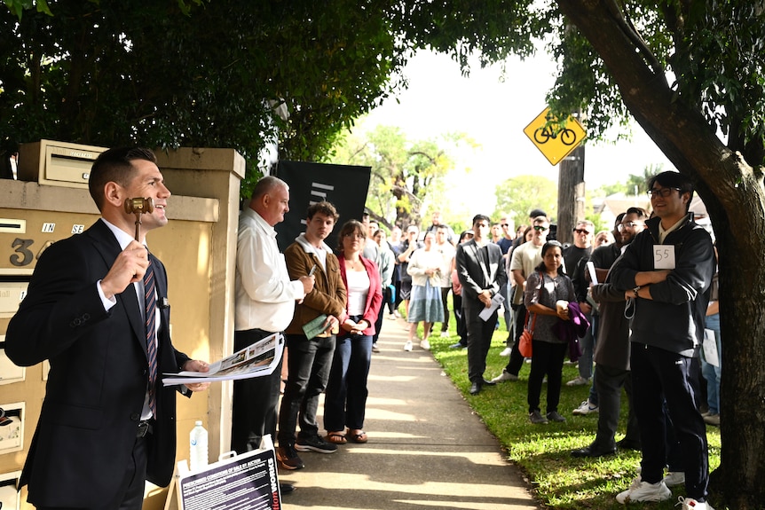 An auction agent trying to sell a home in front of a crowd of three dozen people, outside an apartment complex.