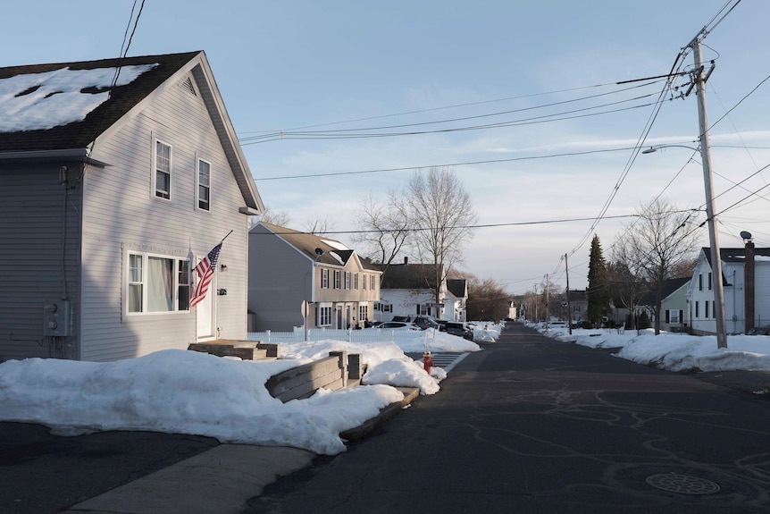 A street of two storey homes, with the footpath and some roofs covered in snow. 