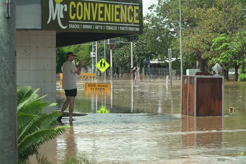 A man takes a photo of a flooded street.