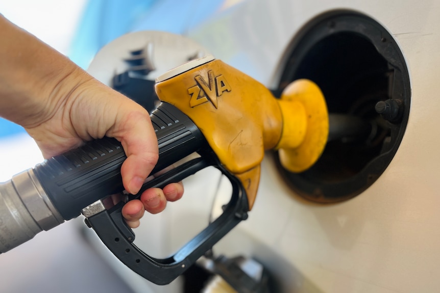 A close up of hand holding a fuel pump at a bowser while filling up car 