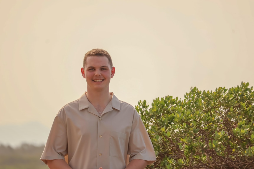 A man stands in front of a bush.