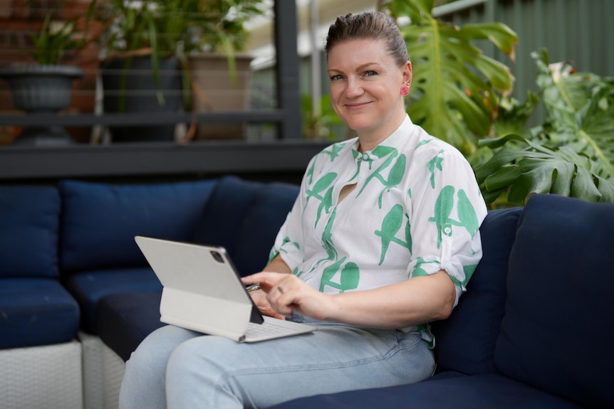 Claire Pullen from Australian Writers' Guild sits on a lounge with a laptop on her knees as she looks at the camera