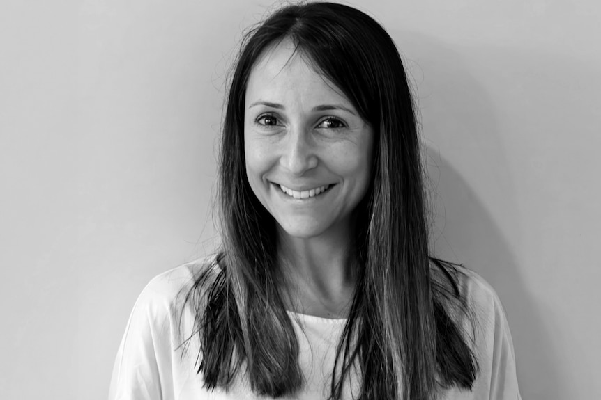A black-and-white photo of a smiling women with long dark hair, wearing a white shirt. 