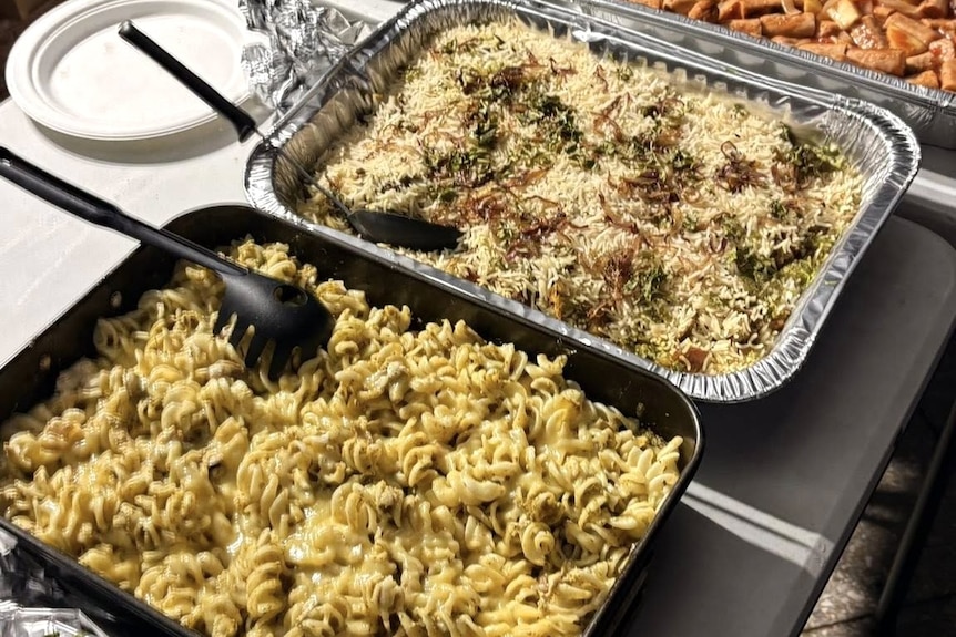 Three large silver trays of hot food like pasta.