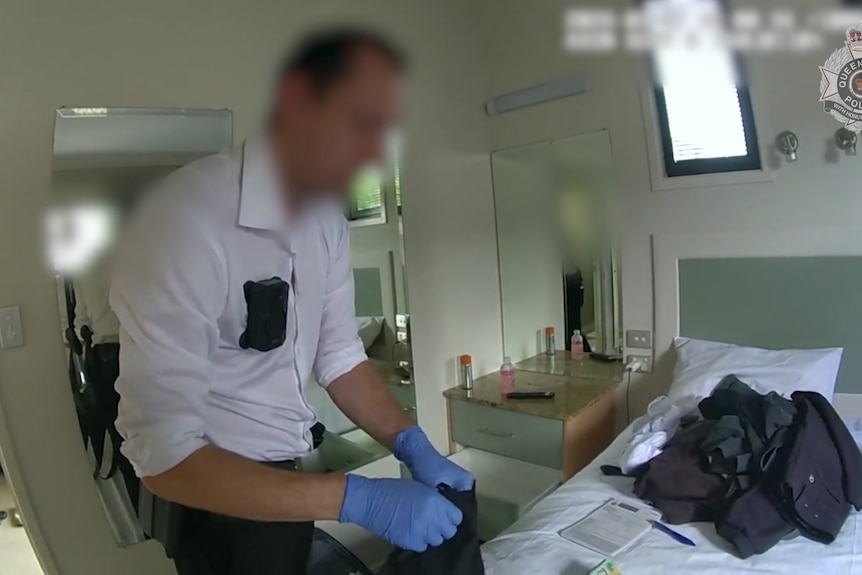 An unidentifiable man in a business shirt and gloves examines items in a residential unit.