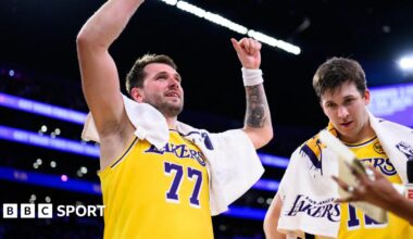 A smiling Luka Doncic celebrates with his arms raised, in the Lakers' yellow vest