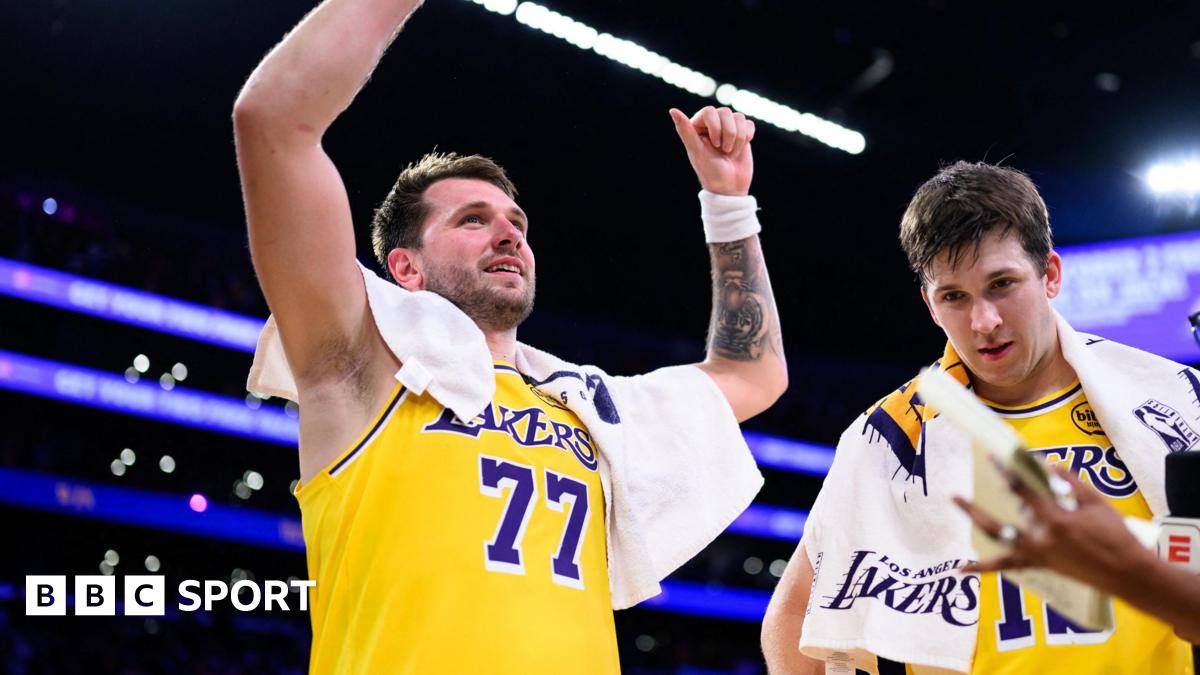 A smiling Luka Doncic celebrates with his arms raised, in the Lakers' yellow vest