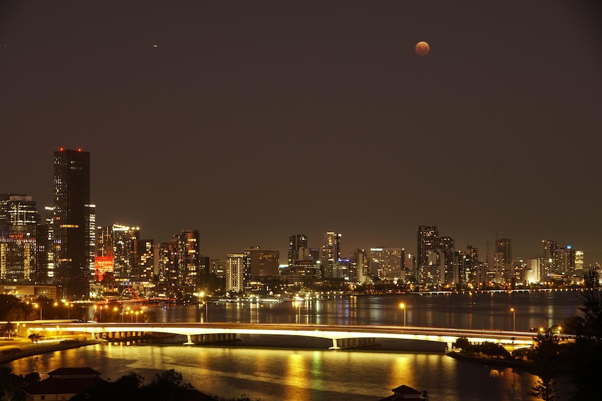 Lit up high-rise buildings at night with a red moon in the sky