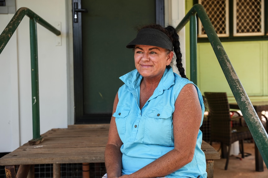 a woman with a visor and blue shirt sitting outside infront of a house