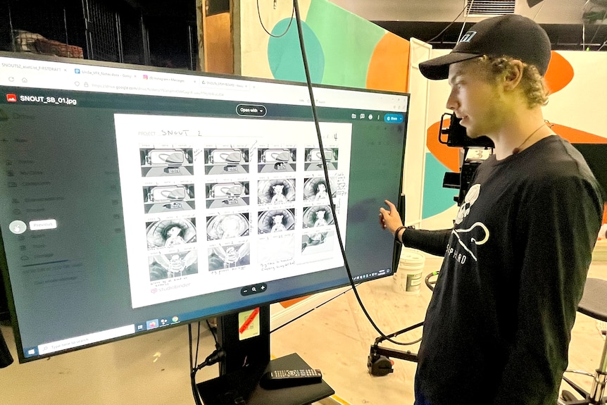 A young man in dark clothes looks at large screen with tiny images on it.