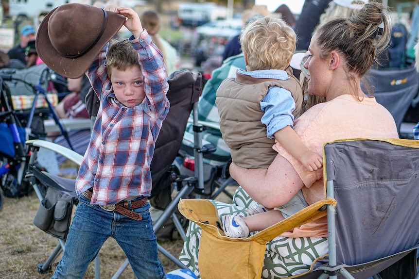 Two young boys. One is held by a woman.