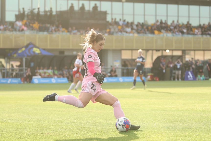 A woman in a pink and white sport uniform kicking a ball.