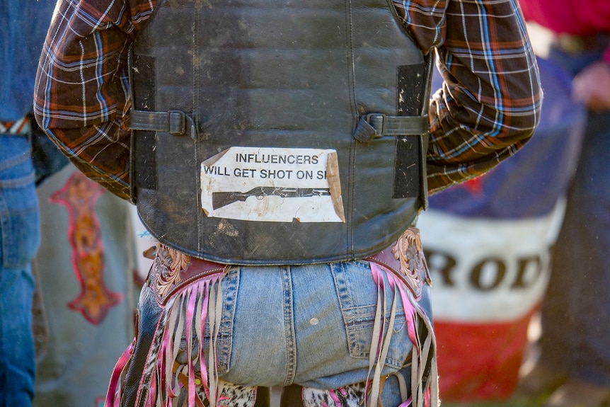 A man wearing a vest with a sticker reading "Influencers will get shot"