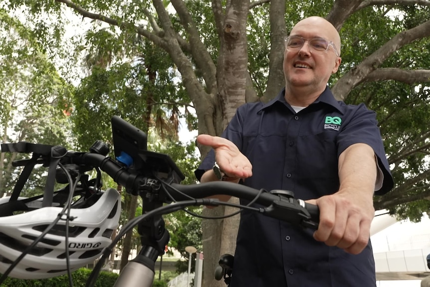 A man stands beside a bike and gesture towards it with his hand.