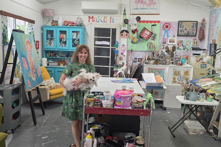 Lady in a green dress holding a dog in her art studio.